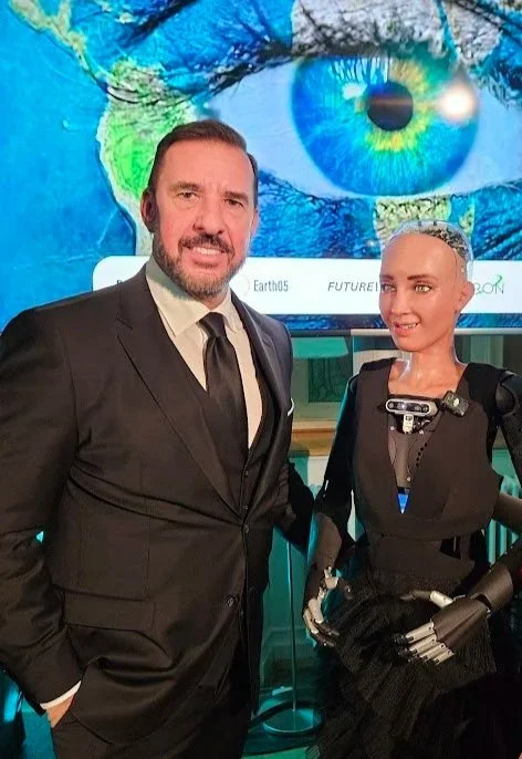 Bill Inman at a technology event with a humanoid robot in front of a world-map display